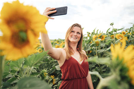 Young Caucasian woman smiling while taking selfie picture with mobile phone in sunflower field
