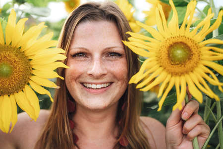 Close up portrait of smiling young woman holding sunflowers at farm during spring seasonの写真素材