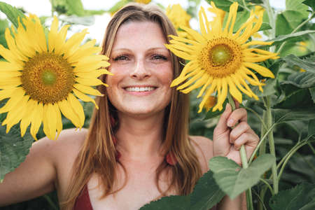 Close up portrait of smiling blond woman holding yellow flowers in sunflower fieldの写真素材