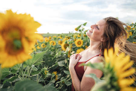 Carefree young woman with blond hair enjoying her vacation in sunflower field on sunny dayの写真素材