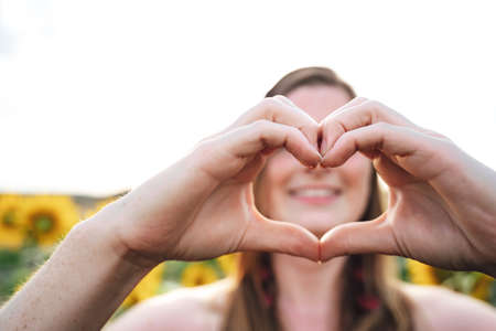 Close up shot of young woman making heart shape with her fingers outdoorsの写真素材