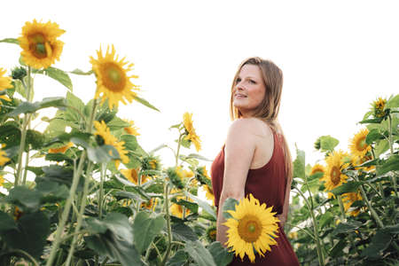 Attractive young woman standing in field of sunflower during spring season against skyの写真素材