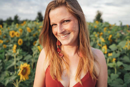 Portrait of smiling blond woman with sunflower plants in background during spring seasonの写真素材
