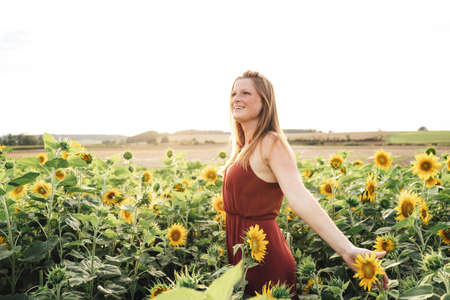 Beautiful young woman enjoying her freedom in sunflower field during spring season against skyの写真素材