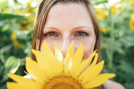 Close up portrait of beautiful young woman hiding her face with yellow sunflowerの写真素材
