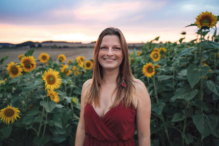 Portrait of smiling young woman standing in sunflower field during sunsetの写真素材