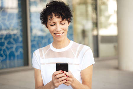 Smiling mature woman text messaging using smartphone outdoorsの写真素材