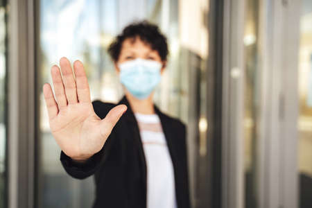 Portrait of mature businesswoman wearing face mask and showing her palm during COVID-19 outbreak representing stopの写真素材