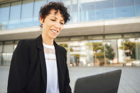 Confident female entrepreneur wearing suit while working on laptop outside officeの写真素材