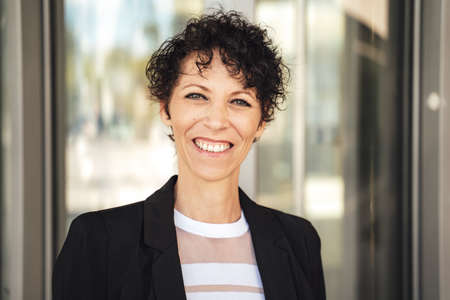 Close up portrait of smiling mature business woman in suit standing outside officeの写真素材
