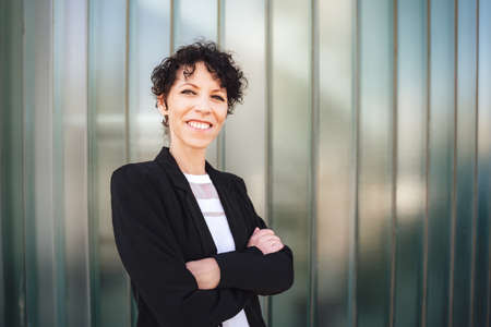 Portrait of smiling female entrepreneur standing arms crossed against green wallの写真素材
