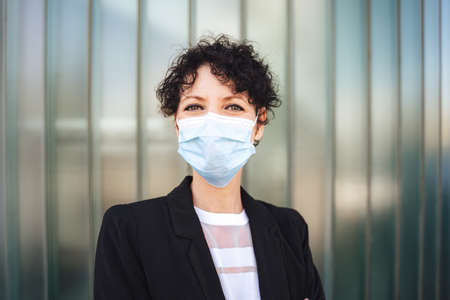 Close up portrait of Caucasian mature businesswoman wearing face mask during COVID-19 outbreak against green wallの写真素材