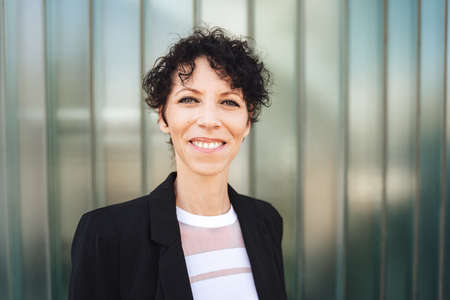 Close up portrait of smiling mature business woman in suit standing against green wallの写真素材