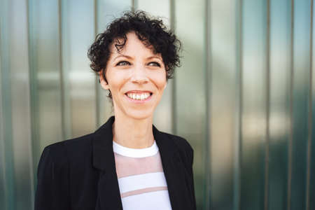 Close up portrait of smiling Caucasian businesswoman looking away while standing against green wallの写真素材