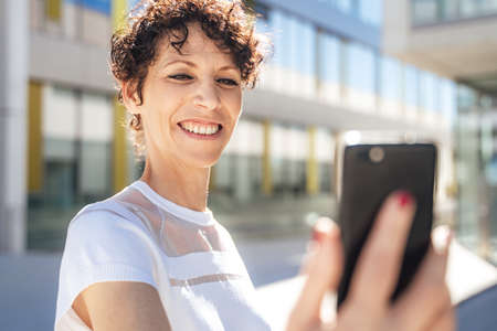 Close up of smiling mature businesswoman having conference call via mobile phone on sunny dayの写真素材