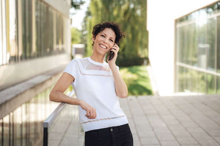 Portrait of smiling mature female entrepreneur talking on mobile phone outside office buildingの写真素材