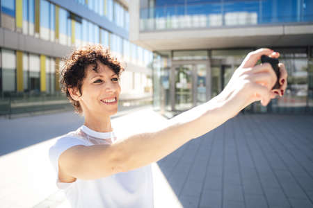 Smiling mature woman taking selfie using mobile phone in city on sunny day during vacationの写真素材