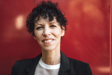 Close up portrait of confident mature business woman in suit against red wallの写真素材