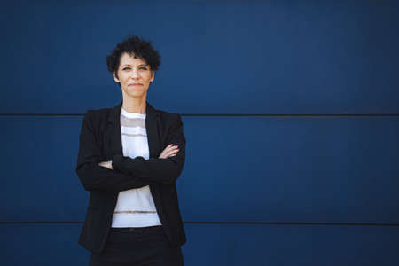 Portrait of confident mature female entrepreneur standing with arms crossed against blue wallの写真素材
