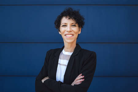 Portrait of smiling mature businesswoman standing arms crossed against blue wallの写真素材