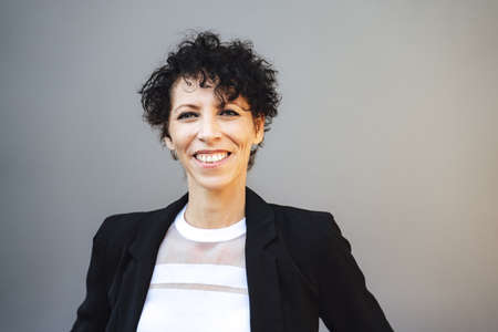 Close up portrait of smiling mature businesswoman in suit against gray backgroundの写真素材