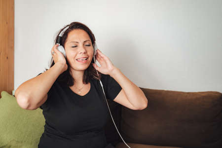 Beautiful Caucasian woman listening music through headphones in living room at homeの写真素材