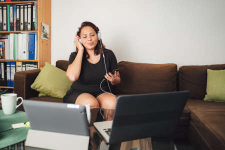 Caucasian female freelancer listening music through headphones after work in living room at homeの写真素材