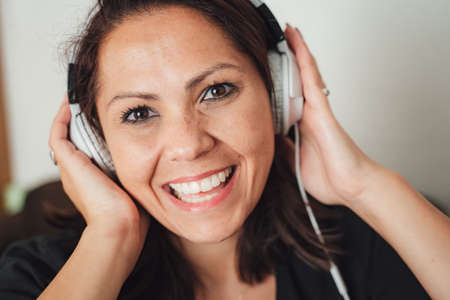 Close up portrait of happy and beautiful woman wearing headphones while enjoying music at homeの写真素材