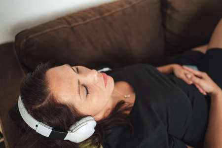 High angle close up of relaxed mid adult woman listening music through headphones while lying on sofaの写真素材