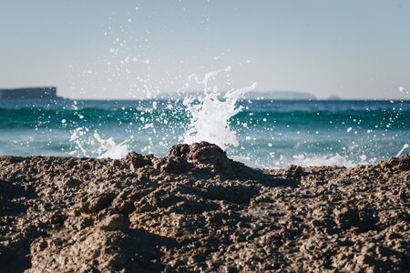 Wave splashing over rocks on Baleal island with Peniche peninsula in the backdropの写真素材