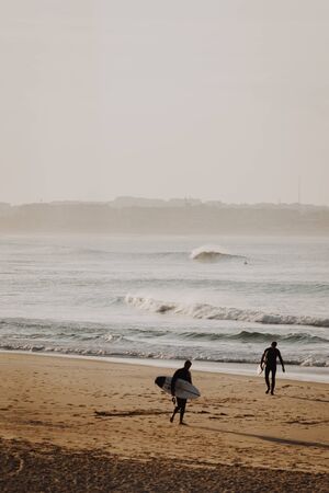 2 surfers walking on the beach after their surf session at the end of the dayの写真素材