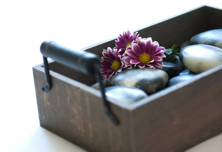 Beautiful wooden box with handles and stones for spa and massage with pink flower on white, soft backgroundの写真素材