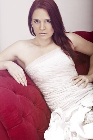 young red haired beautiful bride on red sofa の写真素材