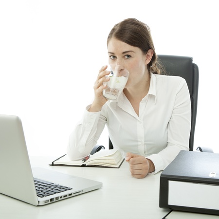 young brunette business woman is drinking water in front of deskの写真素材