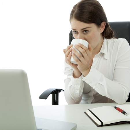 young brunette business woman drink coffee in front of computerの写真素材