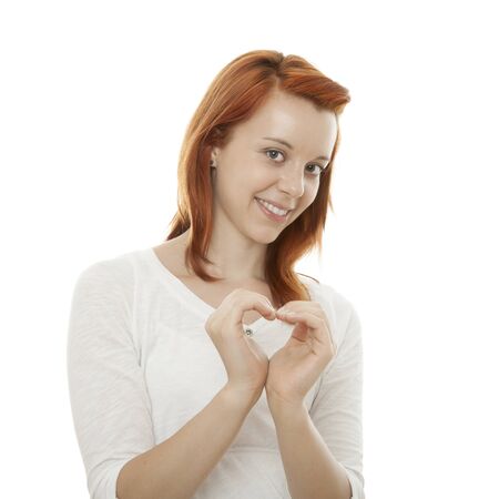young beautiful red haired girl forming a heart of her hands in front of white backgroundの写真素材