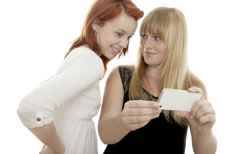 young beautiful red and blond haired girls showing something on cell phone in front of white backgroundの写真素材