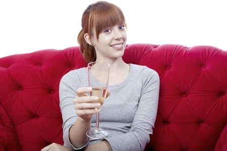 young beautiful red haired girl on red sofa cheers with you in front of white backgroundの写真素材