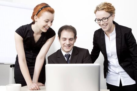 Three happy business colleagues, a business man and two women, looking at the screen of a laptop together and smiling in amusementの写真素材