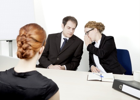 View over the shoulder of a redhead female applicant of two personnel managers conducting a job interview whispering amongst themselves about their impression and decisionの写真素材