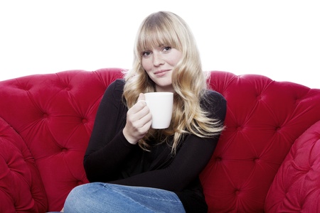 young blond haired girl drink cup of coffee on red sofa in front of white backgroundの写真素材