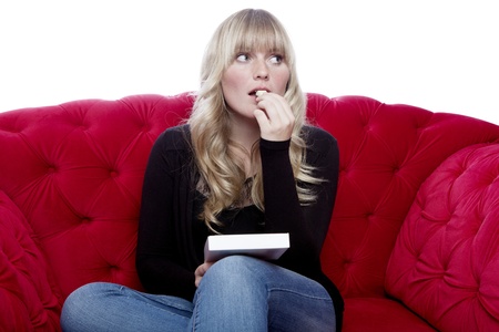 young blond haired girl taste chocolate on red sofa in front of white backgroundの写真素材