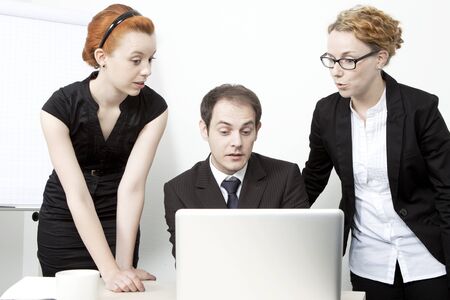 Surprised business team consisting of two women and a man gathered around a laptop computer reacting in surprise to data on the screenの写真素材