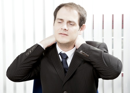 Businessman with a stiff neck or tension headache holding his hands behind his head while grimacing in painの写真素材