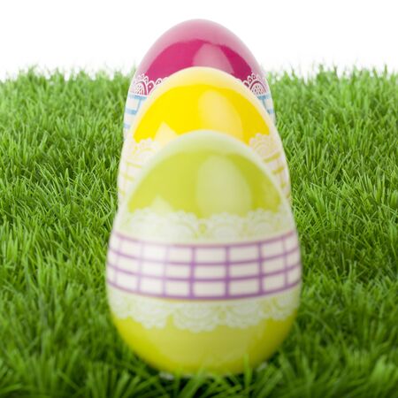 Three shiny reflective vibrant colourful Easter eggs decorated with a lacy ribbon design arranged in a receding row on green grassの写真素材