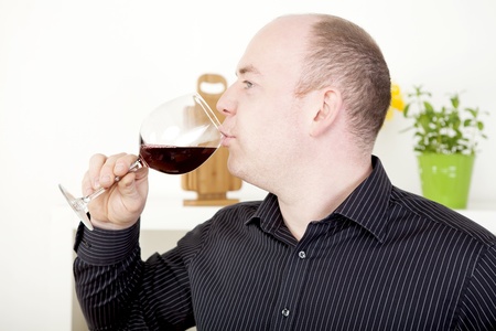 Man standing sideways to the camera enjoying a glass of red wine sipping elegantly from a wineglassの写真素材