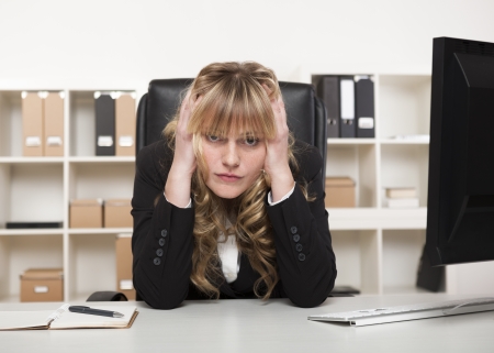 Businesswoman at her wits end sitting at her desk in the office holding her head in both hands and glaring at the cameraの写真素材