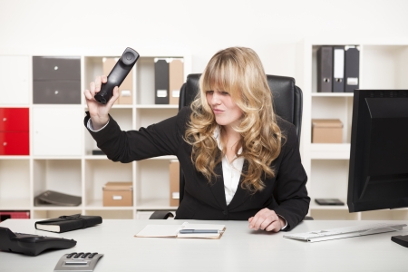 Beautiful young blond businesswoman slamming down the phone in her office after an argumentative phone call or in frustrationの写真素材