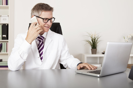 Medical Doctor Talking to Client Using Phone While Reading at Laptopの写真素材