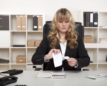 Young businesswoman sitting at her desk with a look of stern concentration tearing up a document showing her displeasureの写真素材